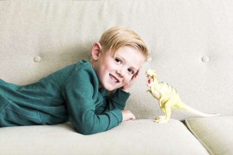 Boy (2-3) lying on sofa with toy dinosaur