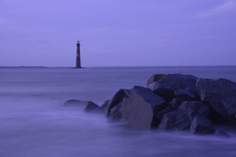 Coastal rocks and lighthouse silhouetted as dusk