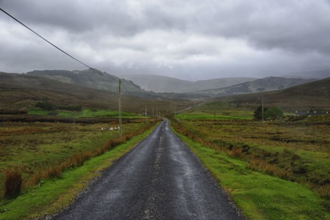 Landscape with asphalt road and green grass, clouds in sky, hills in background