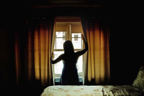 Rear view of female opening curtains at bedroom window