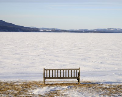 Park bench at edge of a frozen snowed lake, hills in background