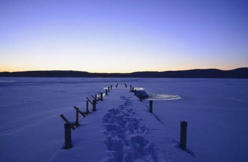Symmetrical image of snowed jetty with footprints at dawn, hills on horizon