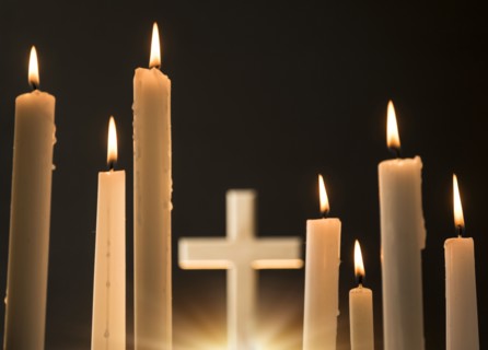 Burning candles with cross in background.