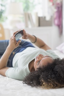 Teenage girl (16-17) texting in bedroom.