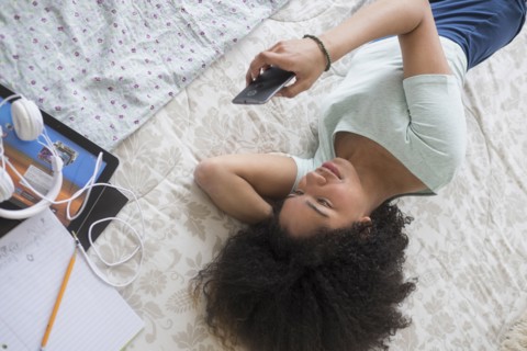 Teenage girl (16-17) texting in bedroom.