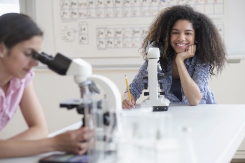Teenage girls (14-15, 16-17) using microscope in science class.