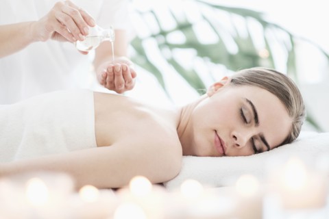Therapist putting massaging oil on young woman in spa.