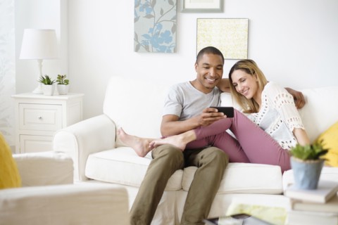 Mid adult couple looking at smart phone in living room.