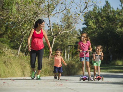 Pregnant mother and children (2-3, 6-7, 8-9) walking outdoors
