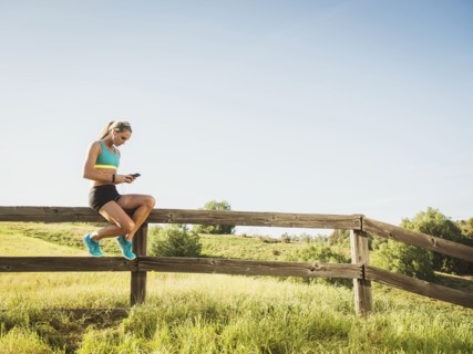 Woman sitting on fence, using smart phone