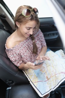 Woman checking phone in car with map on lap.