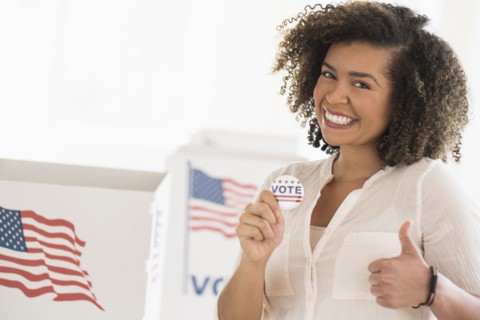 Young woman holding voting badge and smiling.