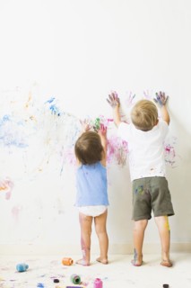 Children (2-3) painting on wall, rear view