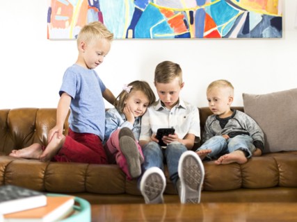 Children (2-3, 4-5, 6-7) sitting on sofa and using smartphone