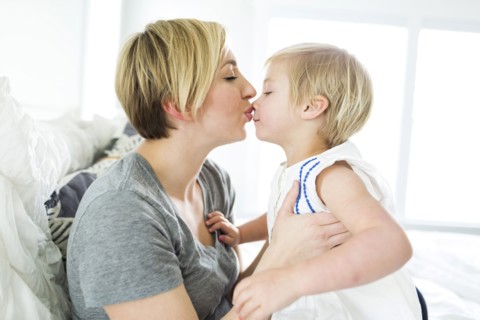Woman kissing girl (2-3) in bedroom