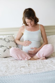Smiling pregnant woman sitting on bed.