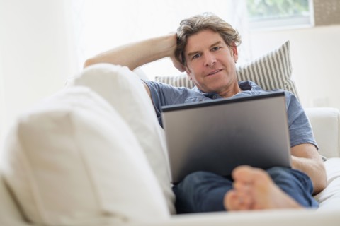 Mature man using laptop on sofa.