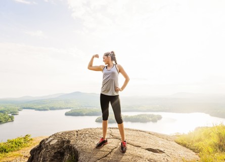 Young woman standing on top of mountain and flexing muscles