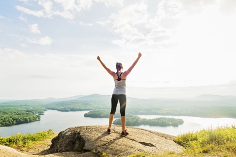 Young woman standing on top of mountain with outstretched arms, rear view