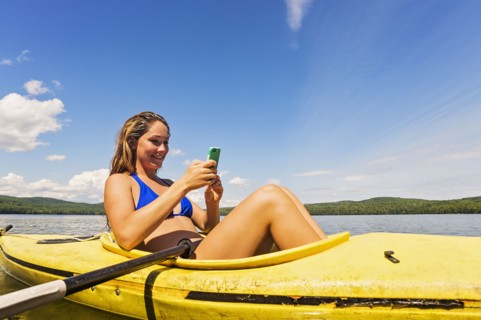 Young woman using Smartphone in kayak on lake