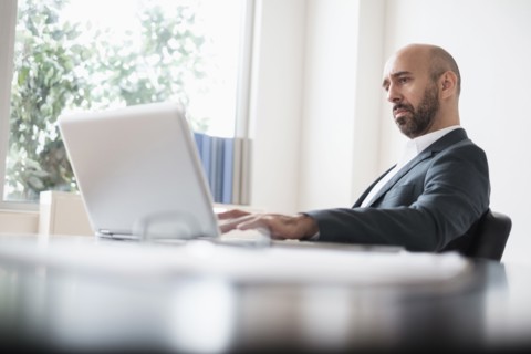 Concentrated businessman working with laptop at desk in office.