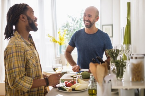 Smiley homosexual couple drinking wine in kitchen.