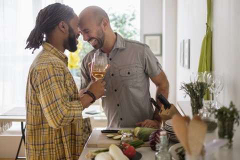 Smiley homosexual couple drinking wine in kitchen.