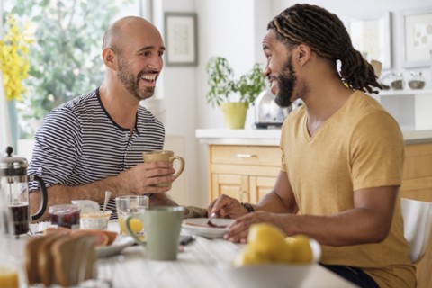 Smiley homosexual couple having breakfast in kitchen.