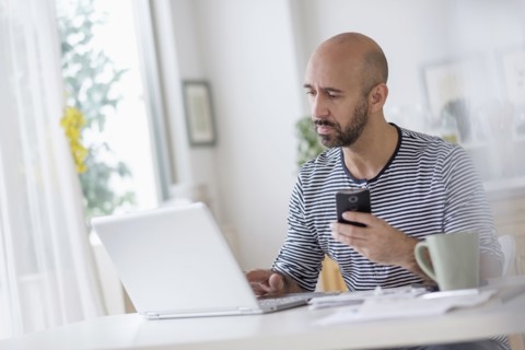 Man working with laptop and holding smart phone at table.