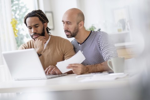 Two men working with laptop at table at home.
