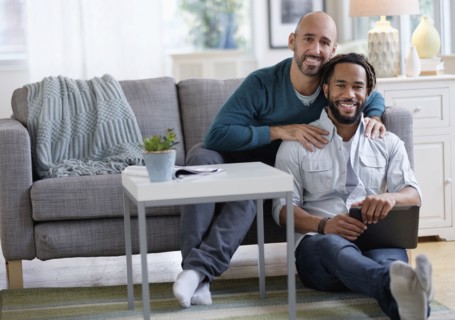 Man massaging boyfriend by sofa in living room.