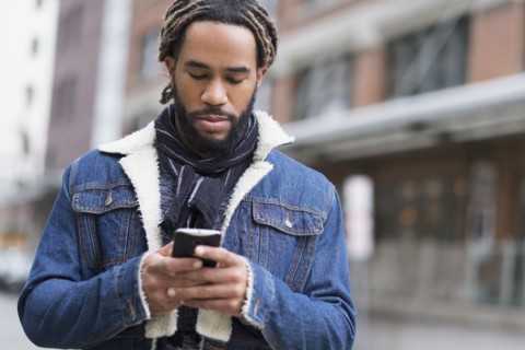 Serious man with dreadlocks using smart phone in street.