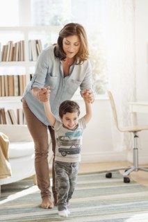 Mother holding son (2-3) making first steps.