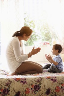 Mother playing with son (2-3) on bed.