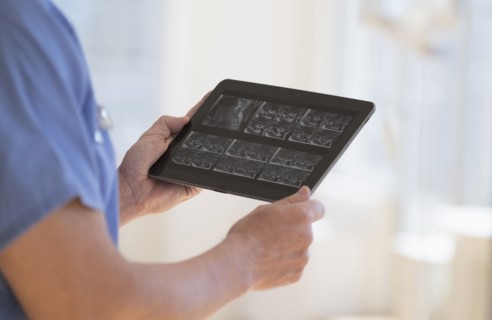 Man in scrubs watching ultrasound results on tablet.