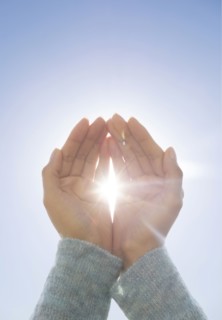 Female hands against clear sky, sun shining through fingers.