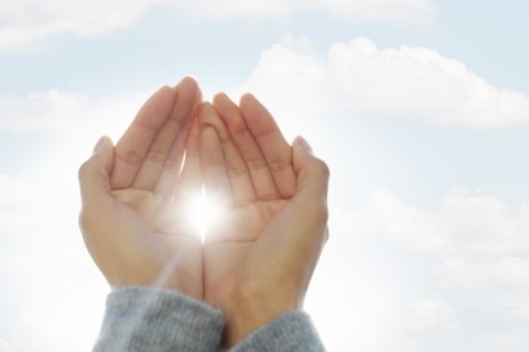 Female hands against clouds, sun shining through fingers.