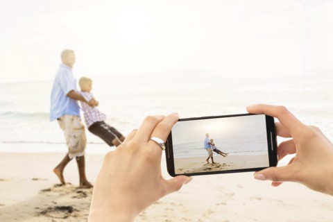 Young woman photographing father with son (12-13) on beach. Jupiter, Florida, USA.
