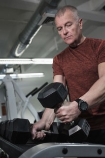 Man in health club picking up dumbbells.