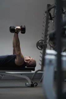 Man exercising with dumbbells on weight bench.