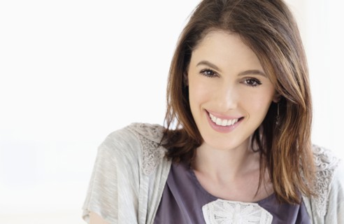 Studio shot portrait of smiling woman with brown hair.
