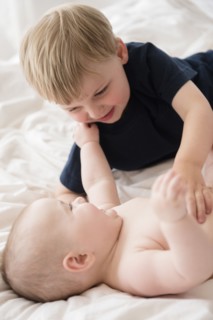 Brother (2-3) playing with baby sister (12-17 months) on bed