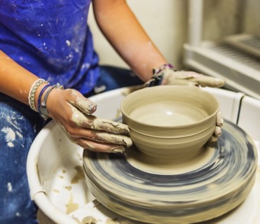 Woman shaping clay bowl on pottery wheel