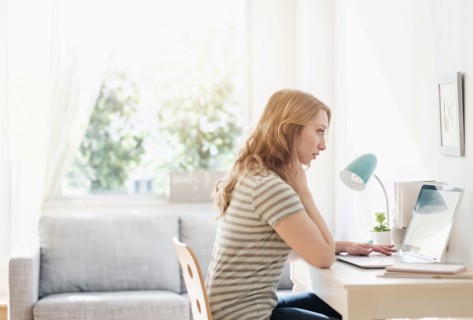 Side-view of young woman working on laptop at home.