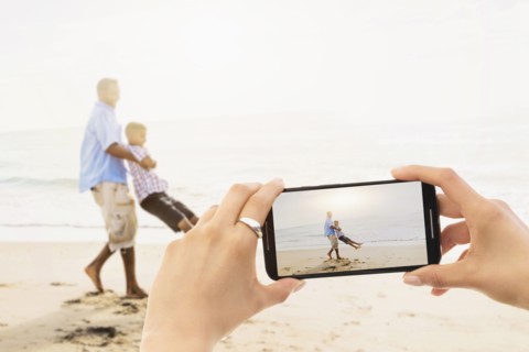 Personal perspective of woman photographing father playing with son (12-13) on beach. Jupiter, Florida, USA.
