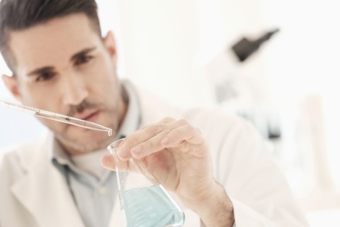 Man pouring liquid into conical flask.