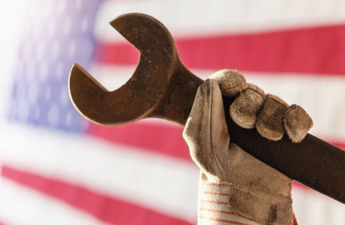 Manual worker's hand holding wrench with American flag in background.
