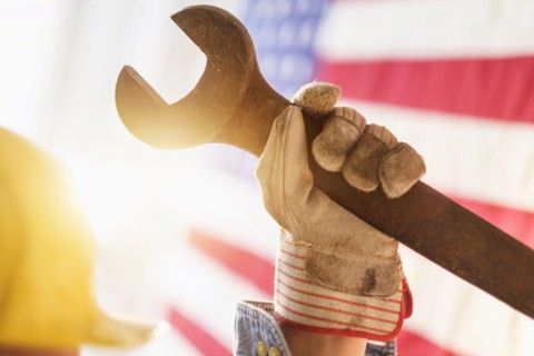 Manual worker's hand holding wrench with American flag in background.