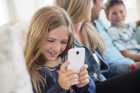 Girl (6-7) sitting on sofa, using smart phone