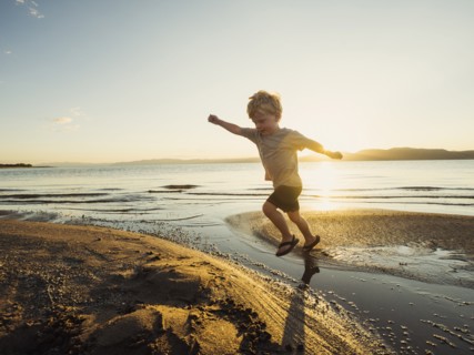Small boy (4-5) jumping over water on sunny day